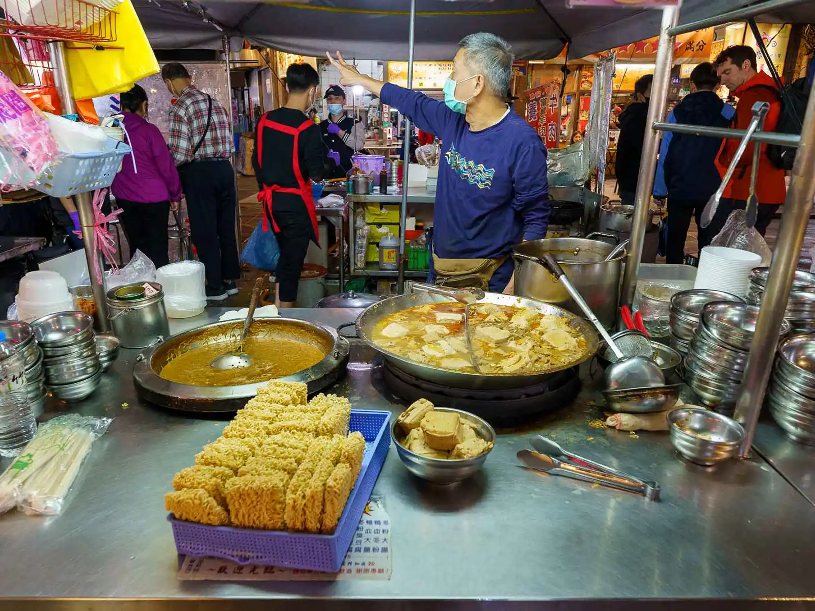 A vendor flashes the peace sign from his stinky tofu stall in a night market.