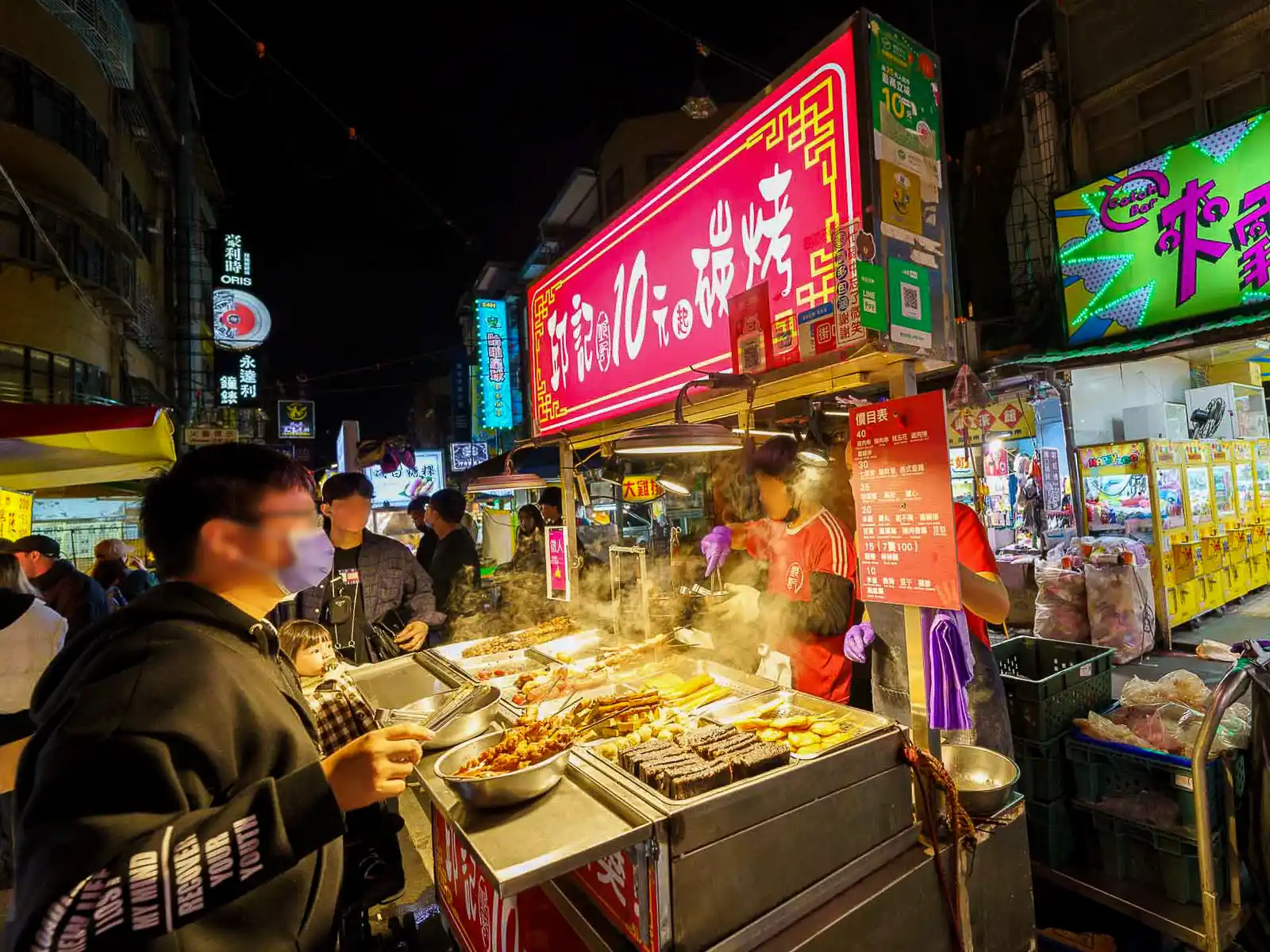 Bustling night market scene with a vendor cooking skewers.