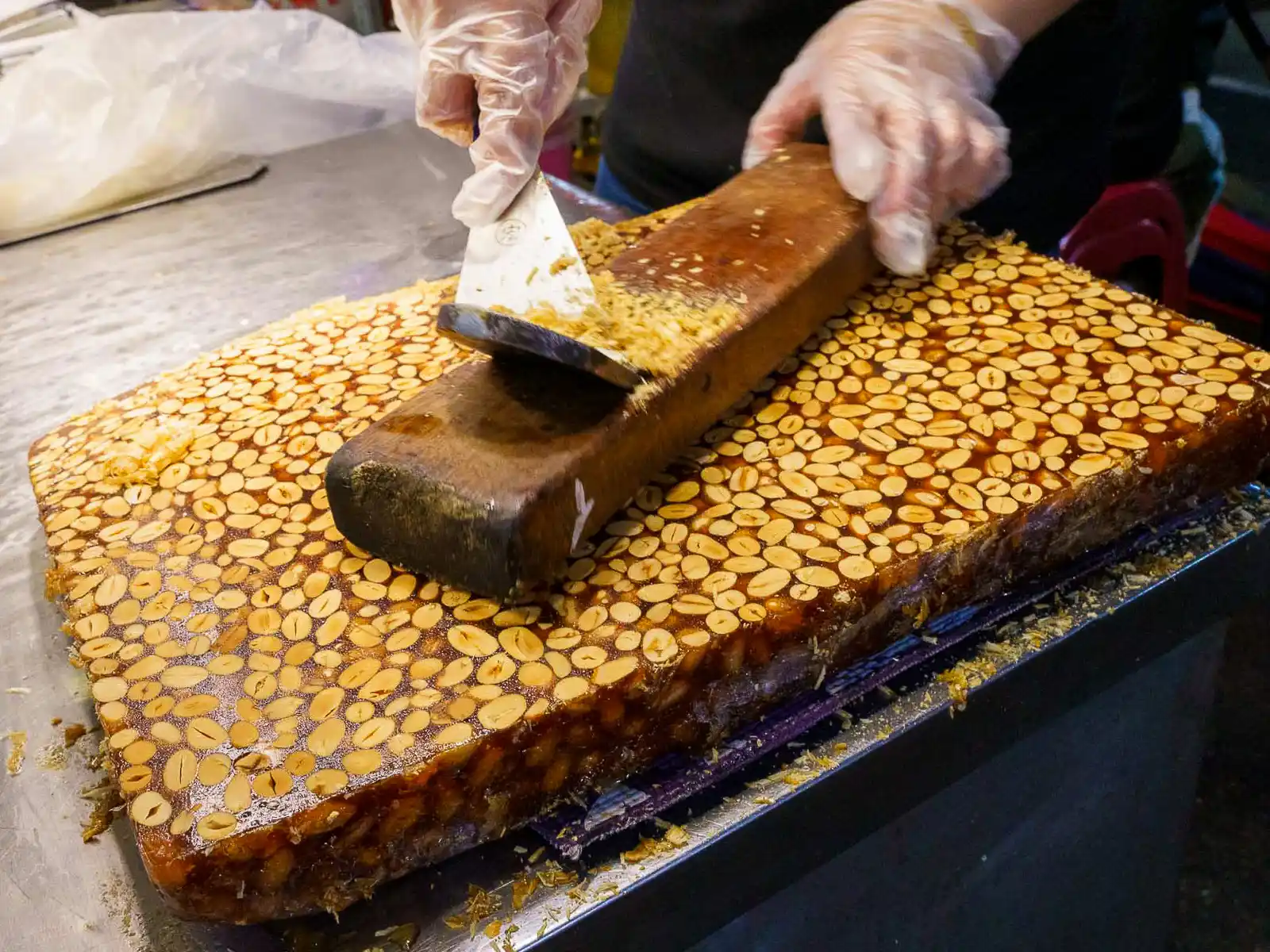 A vendor cuts a large block of peanut candy with almonds.