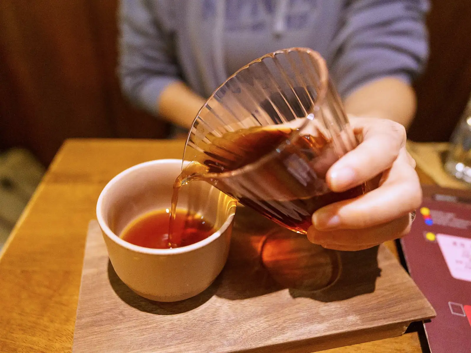 Close-up of a coffee tasting session with a clear glass pouring coffee into a white cup.