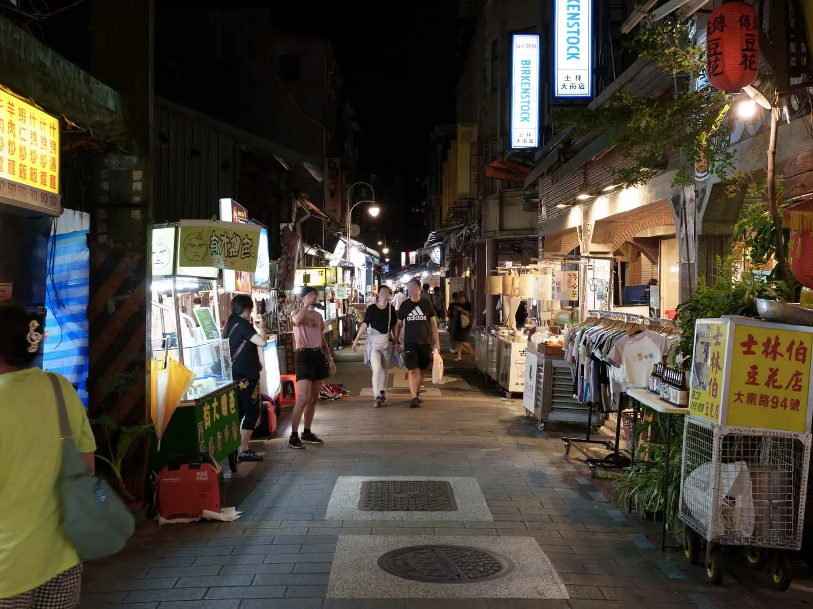 Visitors stroll past food stalls and clothing shops at a bustling Taipei night market.